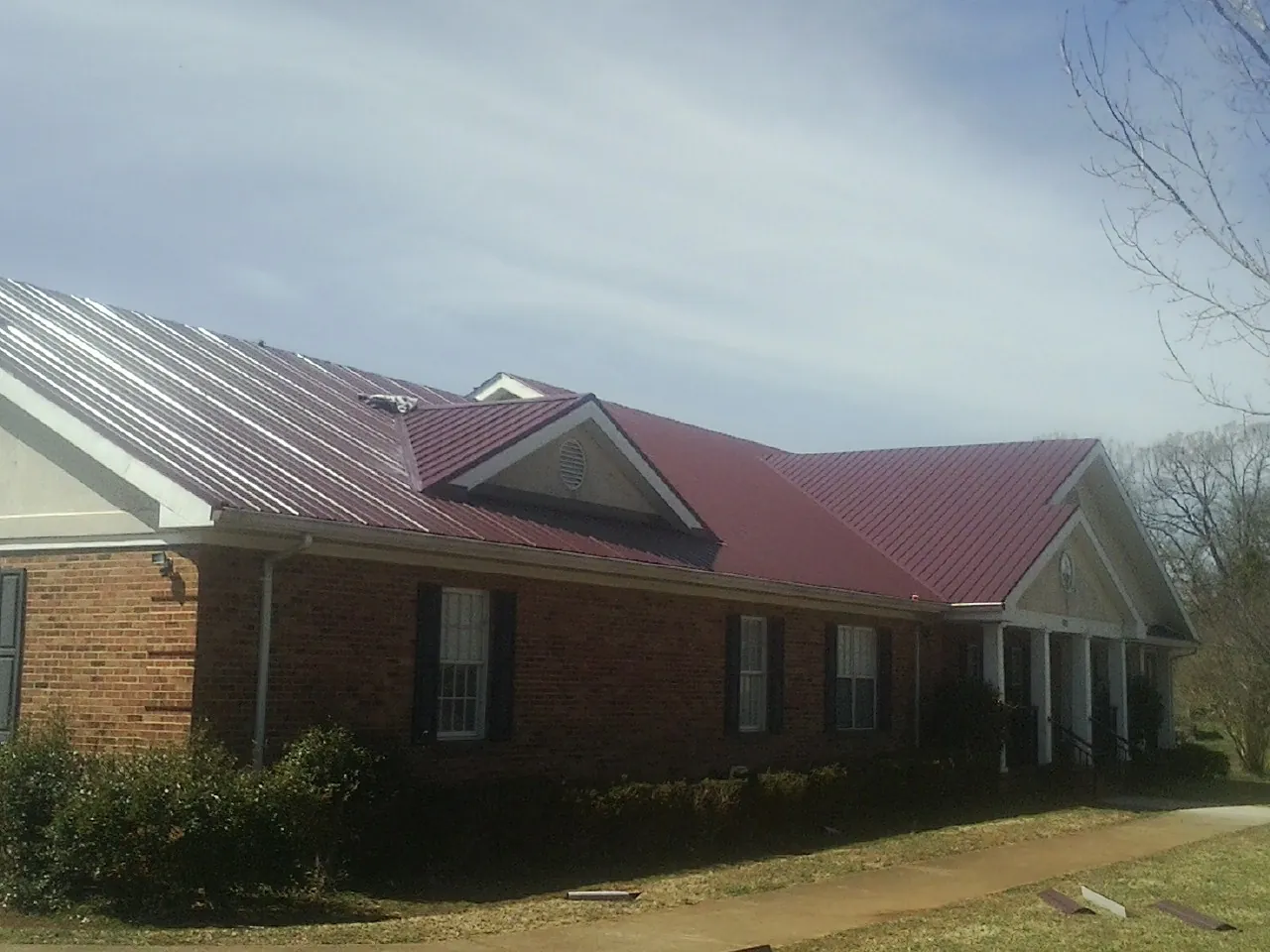 Red metal roof with gabled entries on a long brick building, from a Hail Damage Roof Repair job in Heislerville