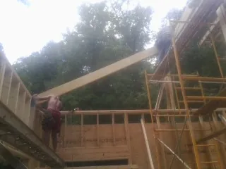 Carpenter raising a rafter beam on a new second story frame in Heislerville