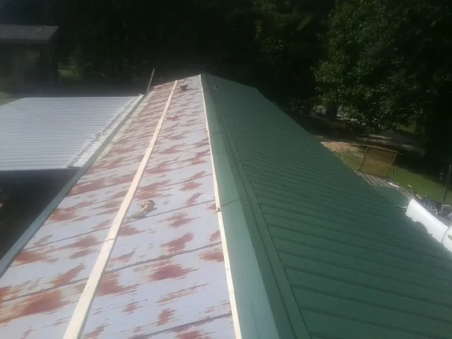 Old rusted panels beside newly installed green metal roofing — Wind Damage Roof Repair by Roofing Brothers in Heislerville