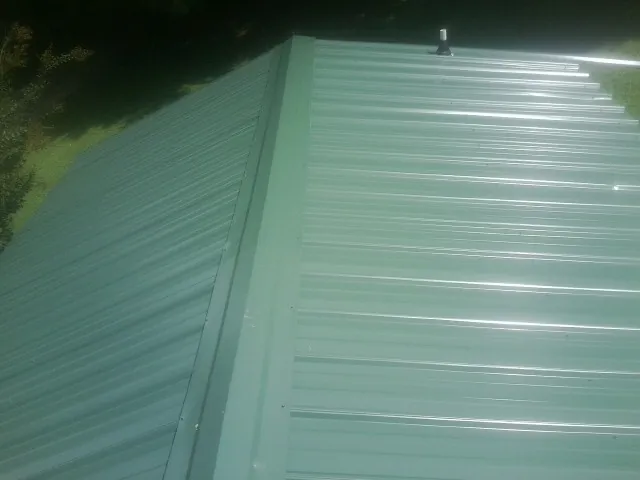 New green metal panels meeting at the ridge of a roof — Flat Roof Repair work by our crew in Heislerville