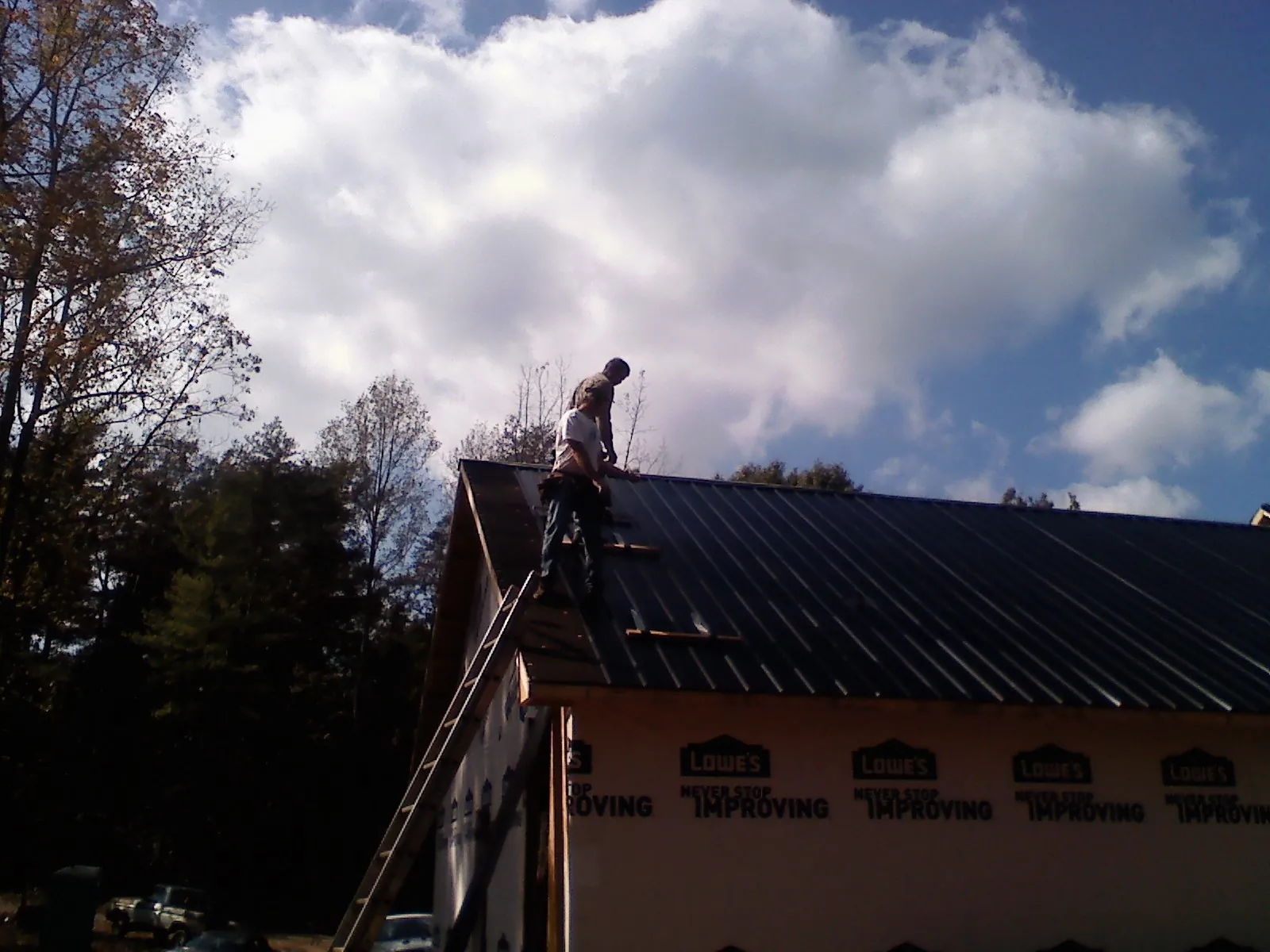 Roofer fastening dark metal panels high against a cloudy sky, from a Roof Inspection job in Heislerville