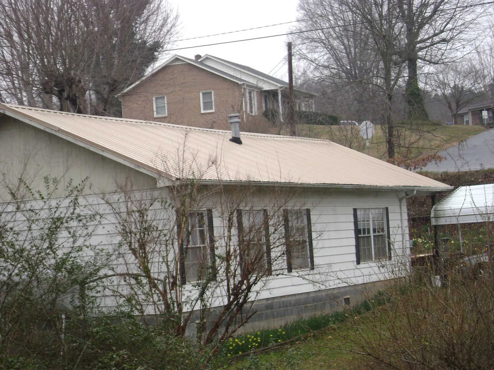 Tan metal roof on a white sided house set into a hillside — Commercial Roofing by Roofing Brothers in Heislerville
